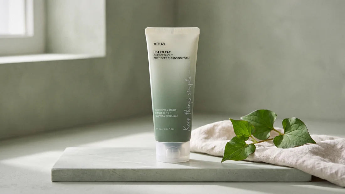 Anua Heartleaf Pore Cleansing Foam standing on pale sage limestone beside folded linen and a sprig of heartleaf, in soft window light