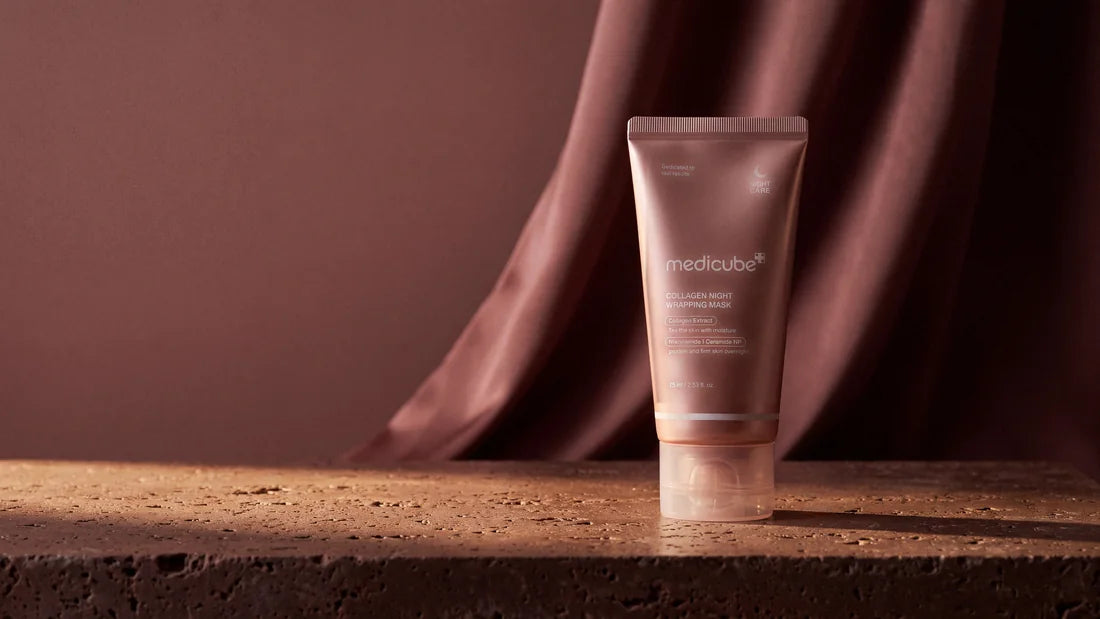 Medicube Collagen Night Wrapping Mask standing on dark travertine before rose-brown silk, in low warm lamplight