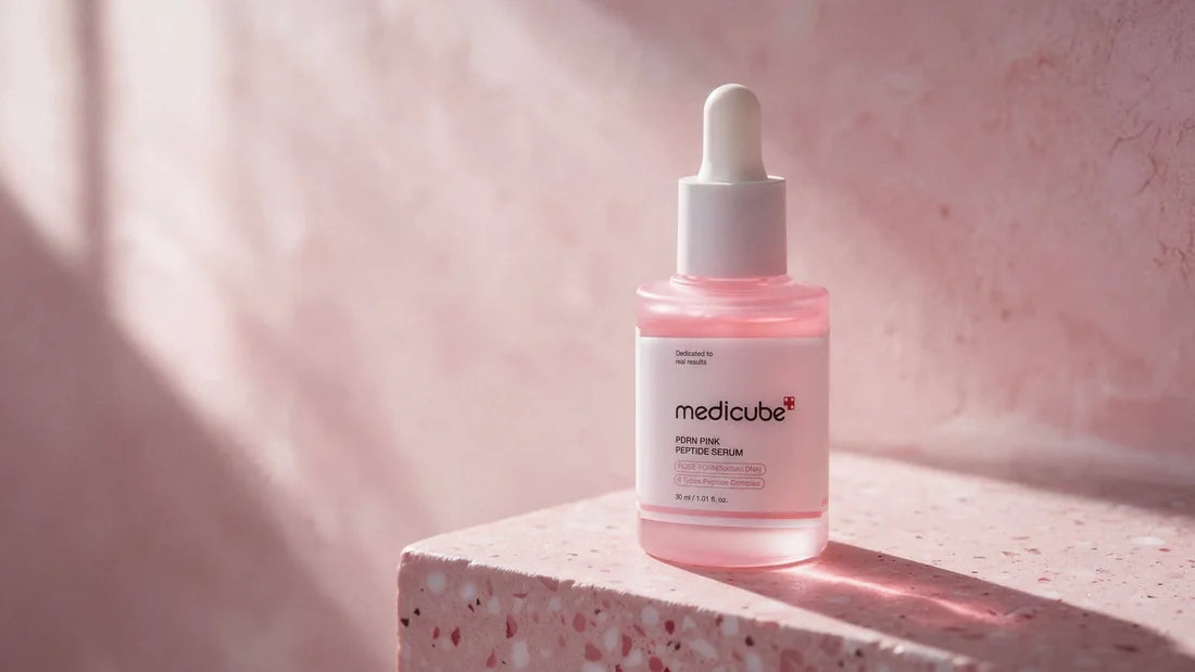 Medicube Pink Peptide Serum dropper bottle on blush-pink terrazzo, in warm sunlight